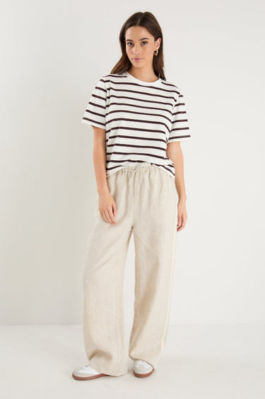 Woman in beige linen pants with side stripe detail and an elastic waistband, paired with a white stripe top. 