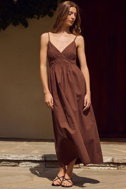 Woman wearing a brown dress standing on a stone path with a dark background