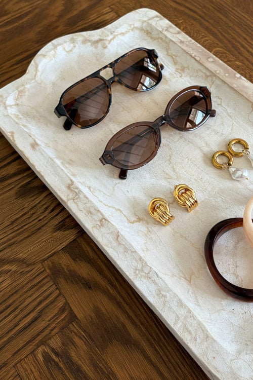 Sunglasses and jewelry on a marble tray with a wooden background