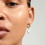 Close-up of a person wearing gold hoop earrings with pearl accents.
