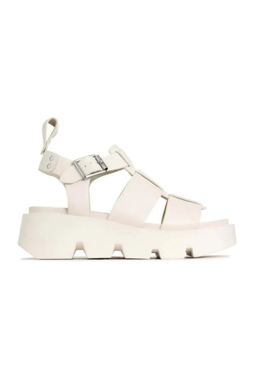 A single platform sandal in a very light cream or off-white color, featuring wide criss-cross straps, a buckle strap on the ankle, and a chunky lug sole, shown against a plain white background.