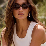 Woman wearing sunglasses and a white tank top outdoors