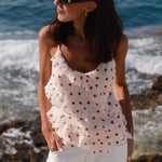 Woman wearing a cream cami top with cherry-red polka dots, ruffled front detailing, and thin adjustable straps
