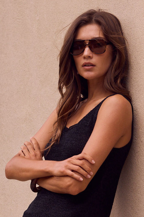Woman wearing sunglasses and a black dress against a beige wall