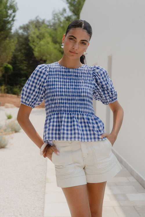 Woman wearing a blue and white checkered top and white shorts outdoors.