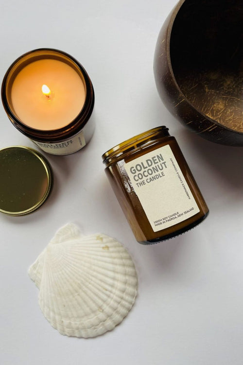 Candle in a jar labeled 'Golden Coconut' with a shell and coconut on a white background