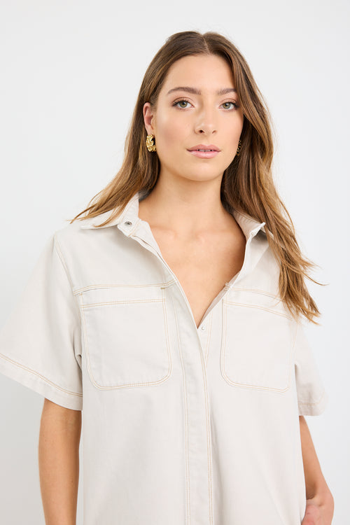 The model wears a ecru denim mini shirt dress with sneakers