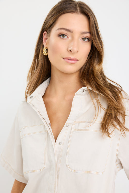 The model wears a ecru denim mini shirt dress with sneakers