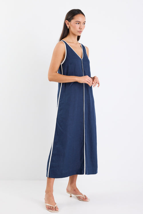 A sleeveless navy dress with ecru contrast piping down the front, featuring side pockets and a relaxed fit. Made from 100% linen for a breathable, comfortable feel.
