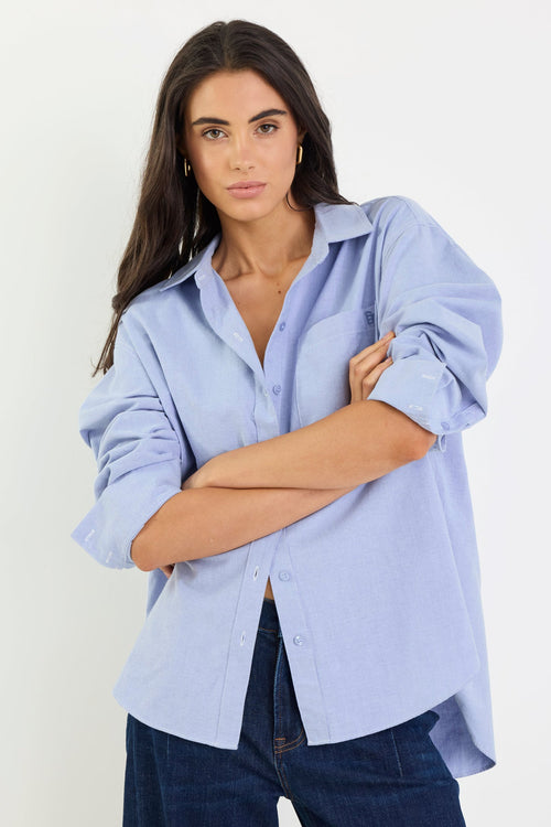 Woman wearing a light blue shirt and dark jeans against a white background