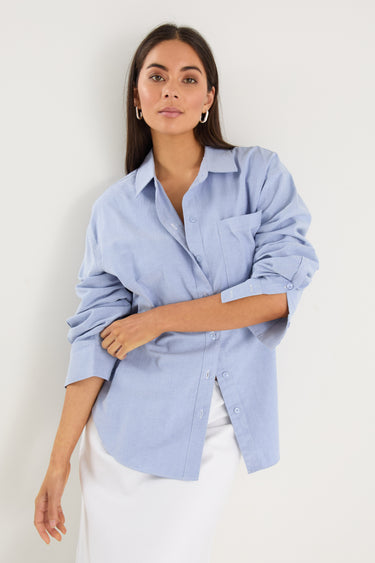 Model wears a blue linen shirt with a white maxi skirt