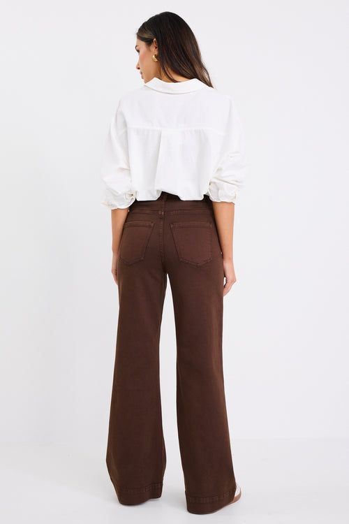 model wears a brown wide jean with a white linen blouse