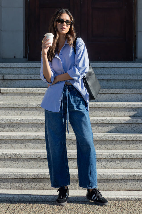 Woman in blue shirt and jeans holding a coffee cup on stone steps.