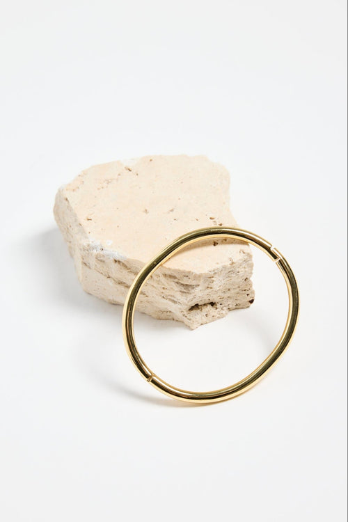 minimalist gold-plated bangle with polished finish and subtle clasp, photographed flat on a white background