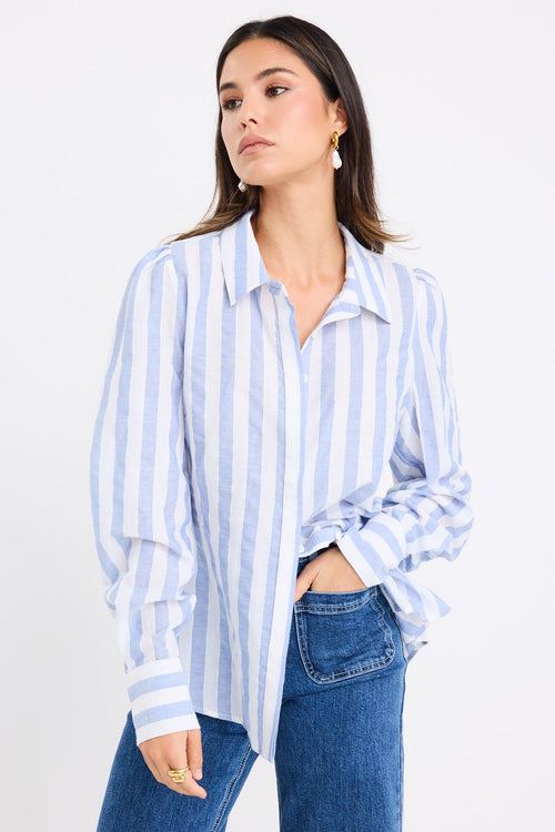 Woman wearing a relaxed blue and white vertical stripe shirt with balloon sleeves, styled casually with wide-leg blue jeans.







