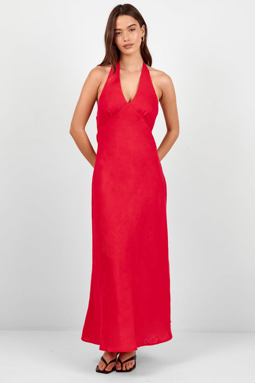 A woman modeling a bright red halter-neck maxi dress with a deep V-neckline and side pockets, paired with black strappy sandals, against a light gray studio background.
col_pattern