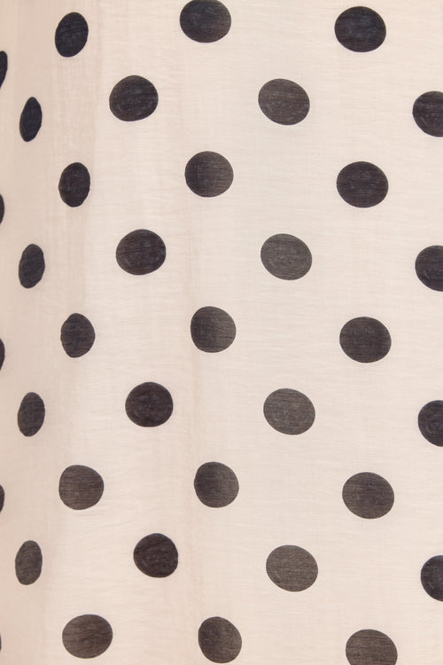 A close-up of a cream-colored fabric with a repeating pattern of large black polka dots.