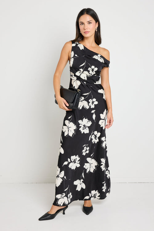 Woman wearing a one-shoulder black floral maxi dress, styled with black heels and a clutch for an elegant evening look.