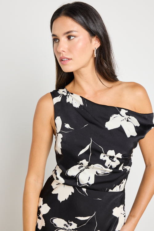 Woman wearing a one-shoulder black floral maxi dress, styled with black heels and a clutch for an elegant evening look.