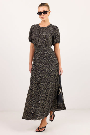 A woman modeling a black and beige animal print maxi dress with puff sleeves, sunglasses, and black sandals against a plain white studio background.