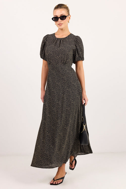 A woman modeling a black and beige animal print maxi dress with puff sleeves, sunglasses, and black sandals against a plain white studio background.