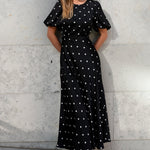 Woman wearing a black dress with white polka dots against a light gray wall.