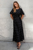 Woman wearing a black dress with white polka dots against a light gray wall.
