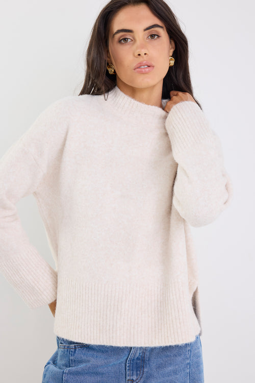 Woman wearing a cream sweater and blue jeans against a white background