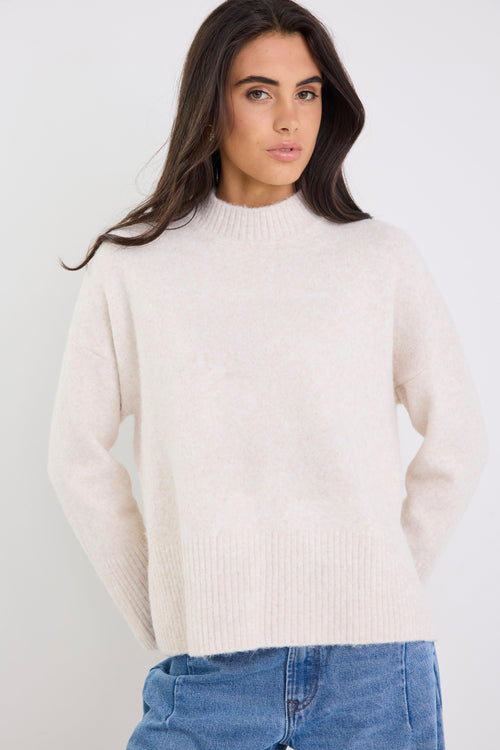 Woman wearing a cream sweater and blue jeans against a white background