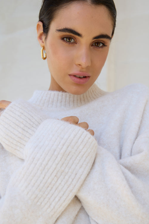 Woman wearing a white ribbed sweater with a plain background