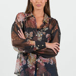 Woman wearing a floral blouse with sheer overlay on a white background