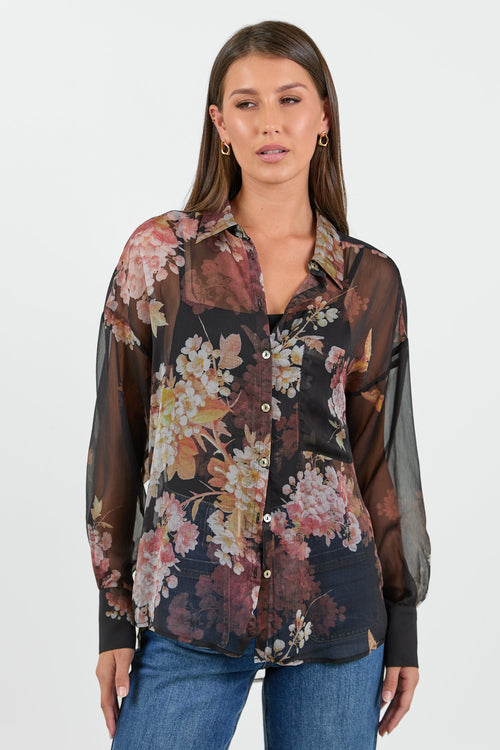 Woman wearing a floral blouse with sheer sleeves on a white background