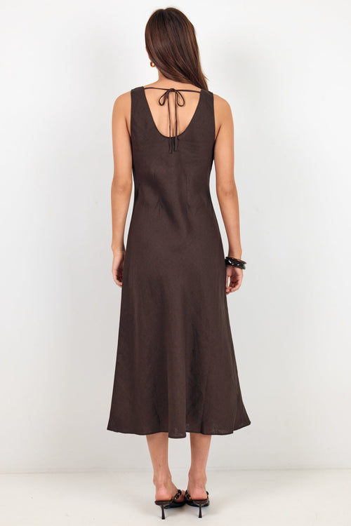 A woman viewed from the back wearing a sleeveless dark brown midi dress with a tie-back neckline and black heels, standing against a plain white studio background.