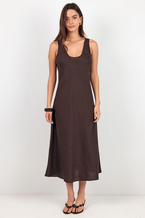 A woman modeling a sleeveless, scoop-neck midi dress in a dark brown color, standing against a plain white studio background.