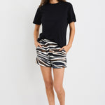 Woman wearing mid-rise chocolate zebra print shorts with an elastic waistband, styled casually with a black top and black sandals.