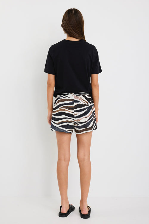 Woman wearing mid-rise chocolate zebra print shorts with an elastic waistband, styled casually with a black top and black sandals.