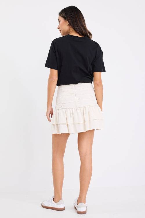 model wears a beige linen ruffle mini skirt with a black t-shirt