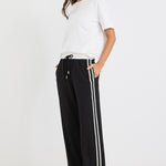 Woman wearing black wide-leg pants with white side stripes, featuring a mid-rise elastic waistband and paired with sneakers.
@col_pattern