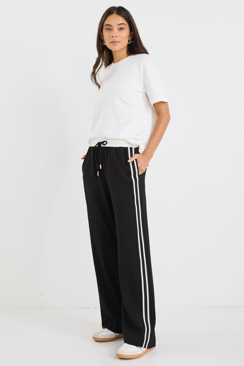 Woman wearing black wide-leg pants with white side stripes, featuring a mid-rise elastic waistband and paired with sneakers.