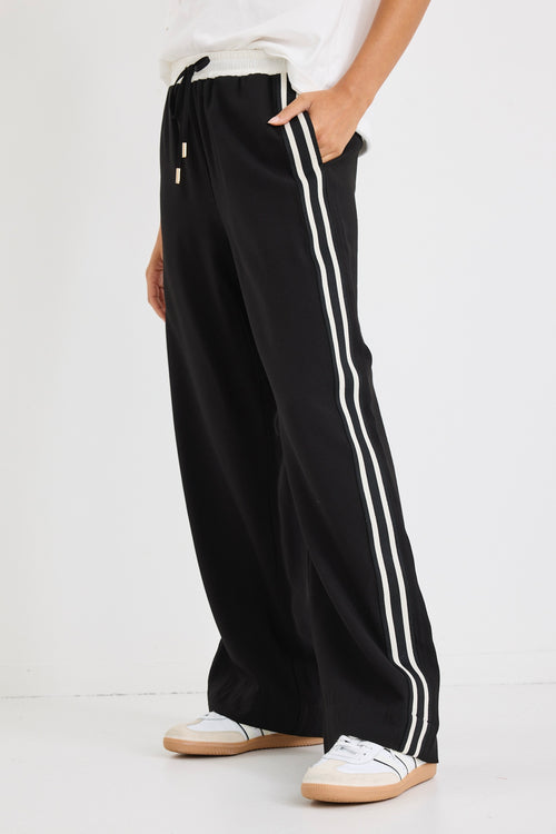Woman wearing black wide-leg pants with white side stripes, featuring a mid-rise elastic waistband and paired with sneakers.