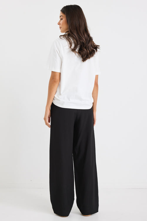Woman wearing black wide-leg pants with white side stripes, featuring a mid-rise elastic waistband and paired with sneakers.