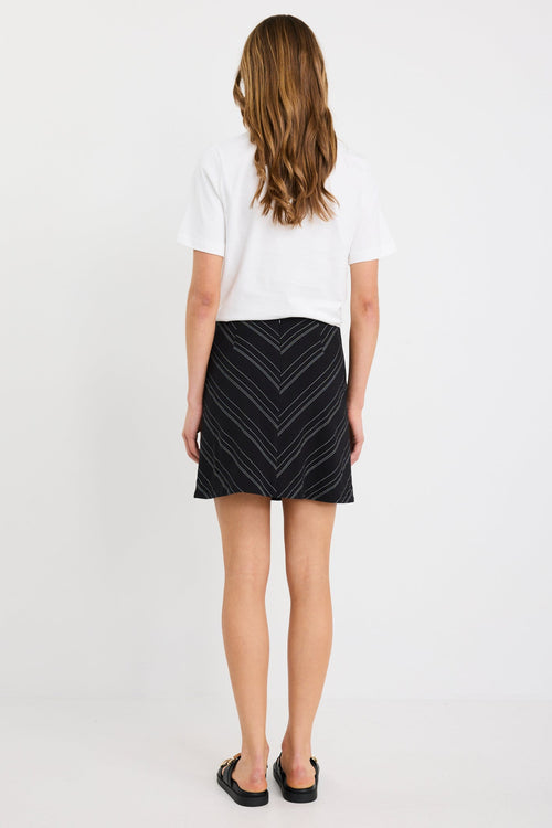 Woman wearing a black and white gradient stripe mini skirt in a chevron pattern, styled with a simple white tee and black sandals.