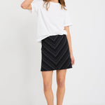 Woman wearing a black and white gradient stripe mini skirt in a chevron pattern, styled with a simple white tee and black sandals.