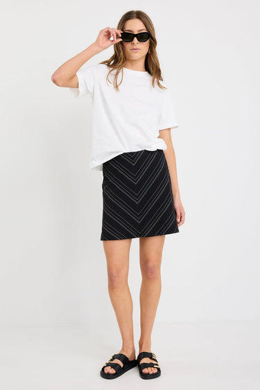 Woman wearing a black and white gradient stripe mini skirt in a chevron pattern, styled with a simple white tee and black sandals.