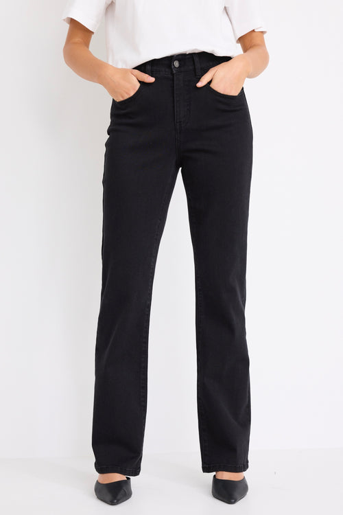 Woman wearing mid-rise, black wash jeans with a plain beige t-shirt and nude sandals.