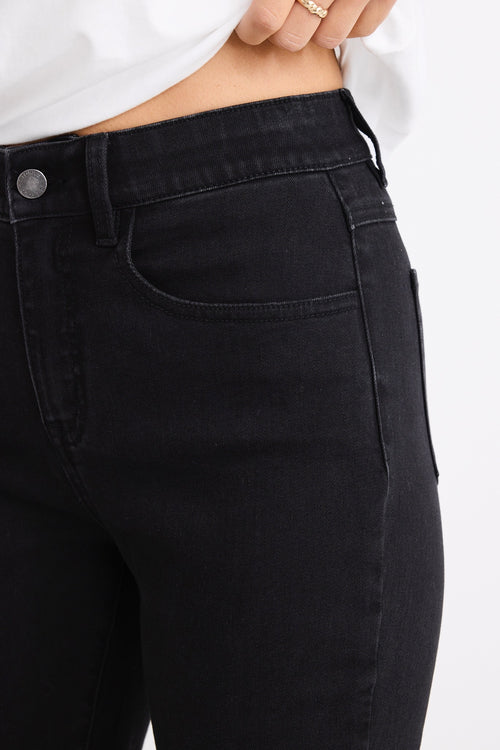 Woman wearing mid-rise, black wash jeans with a plain beige t-shirt and nude sandals.