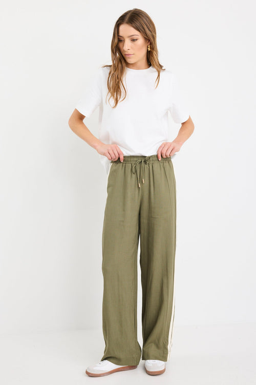 Woman wearing khaki wide-leg drawstring pants with an elastic waist, featuring a relaxed fit and side stripe detail, styled with a plain white tee and white sneakers.
