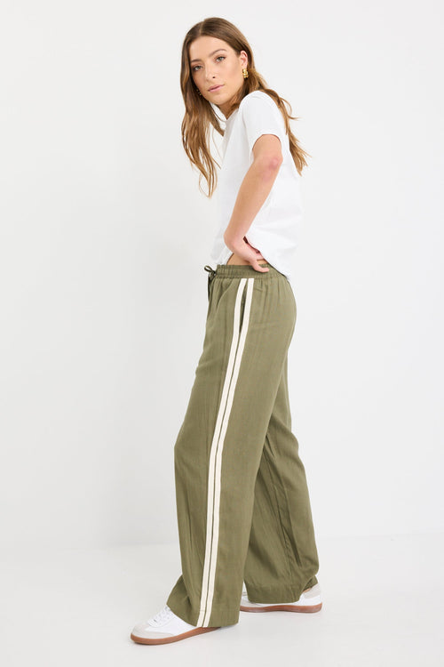 Woman wearing khaki wide-leg drawstring pants with an elastic waist, featuring a relaxed fit and side stripe detail, styled with a plain white tee and white sneakers.