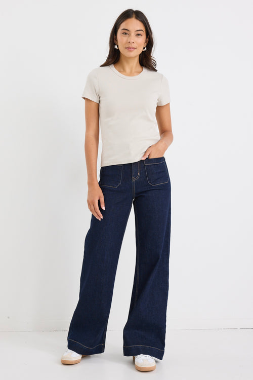 Woman wearing a fitted short sleeve ribbed beige t-shirt with a crew neckline, styled casually with dark blue jeans.