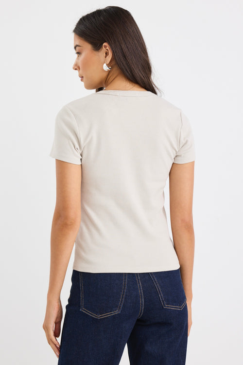 Woman wearing a fitted short sleeve ribbed beige t-shirt with a crew neckline, styled casually with dark blue jeans.